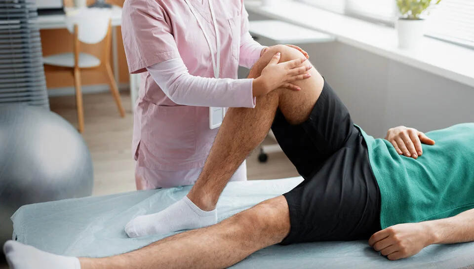 Weight training knee pain evaluation in physical therapy, therapist assessing a patient’s knee range of motion on a treatment table.