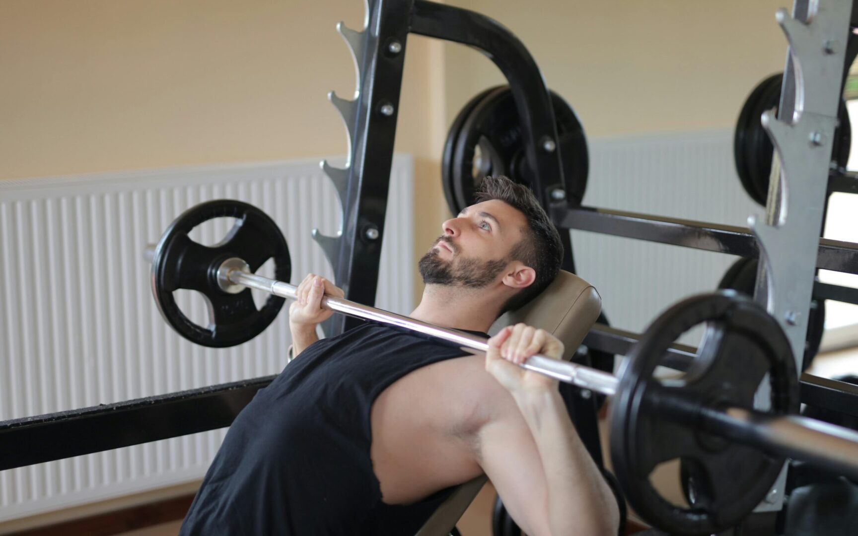 Man performing an incline bench press with a barbell, showing head and neck position to reduce neck pain from bench press.