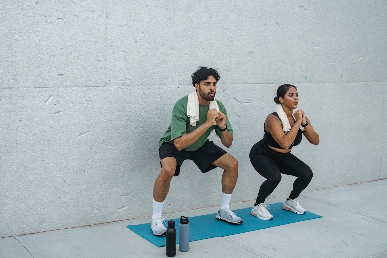 Two people doing bodyweight squats on a mat outdoors, a simple exercise option when thighs hurt after squats.