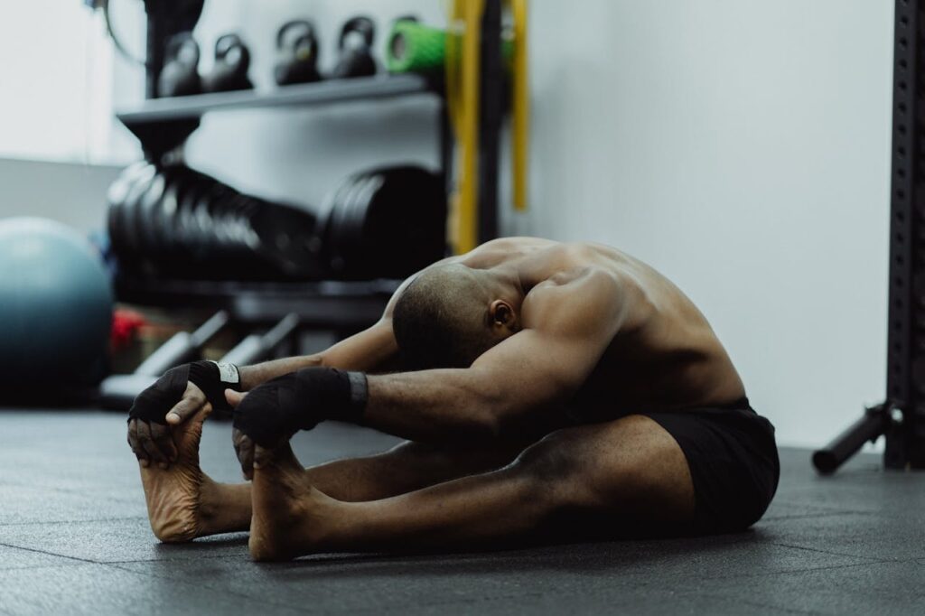 Athlete stretching hamstrings and quads on a gym floor after training, a recovery option when thighs hurt after squats.