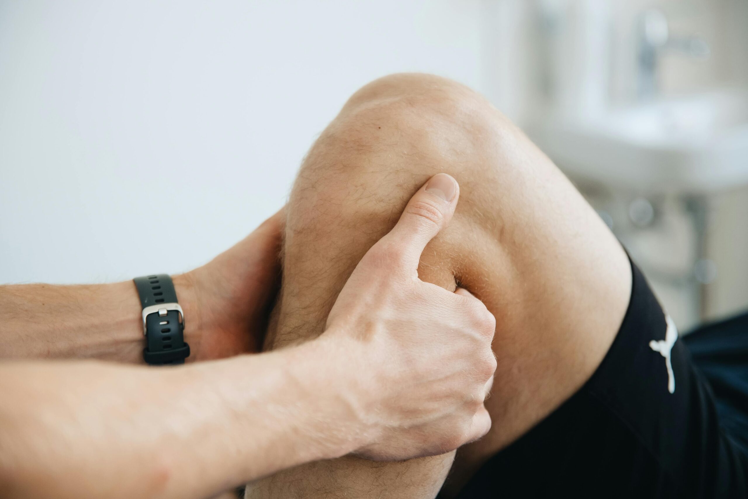 Hands holding a bent knee during an exam, showing physical therapy techniques for knee pain relief and mobility support.